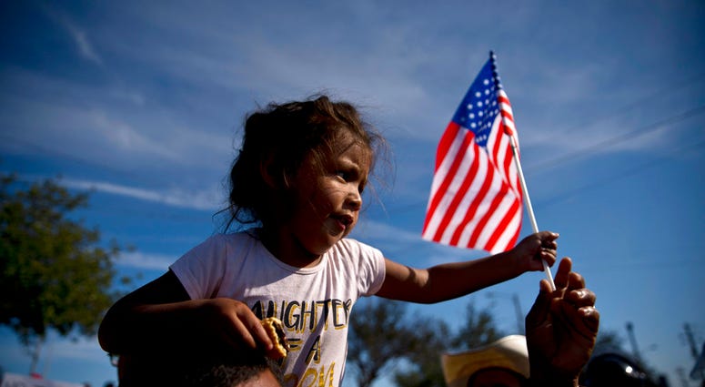 A migrant girl with a U.S. flag sits on the shoulders of a man marching with other migrants to the Chaparral border crossing in Tijuana, Mexico, Sunday, Nov. 25, 2018, as they try to reach the U.S. A migrant girl with a U.S. flag sits on the shoulders of a man marching with other migrants to the Chaparral border crossing in Tijuana, Mexico, Sunday, Nov. 25, 2018, as they try to reach the U.S.