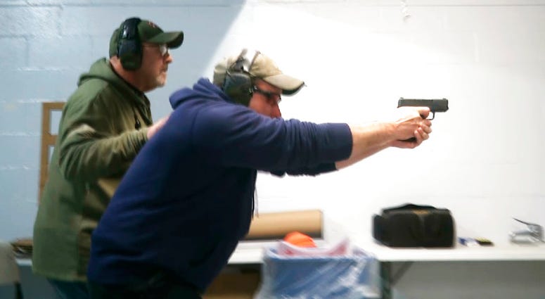 In this photo taken from a video shot on Nov. 28, 2018, Mike Carnevale places his hand on the back of Mark Hennesey while instructing him at the American Tactical Systems' indoor range in Green Island, New York. In this photo taken from a video shot on Nov. 28, 2018, Mike Carnevale places his hand on the back of Mark Hennesey while instructing him at the American Tactical Systems' indoor range in Green Island, New York.