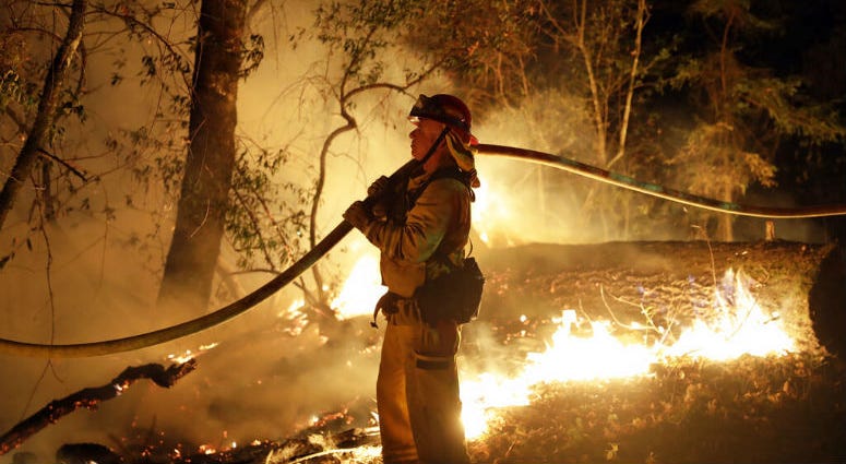 FILE - In this Oct. 14, 2017 file photo, a firefighter holds a water hose while fighting a wildfire in Santa Rosa, Calif. Investigators say the deadly 2017 wildfire that killed 22 people in California's wine country was caused by a private electrical syst FILE - In this Oct. 14, 2017 file photo, a firefighter holds a water hose while fighting a wildfire in Santa Rosa, Calif. Investigators say the deadly 2017 wildfire that killed 22 people in California's wine country was caused by a private electrical syst
