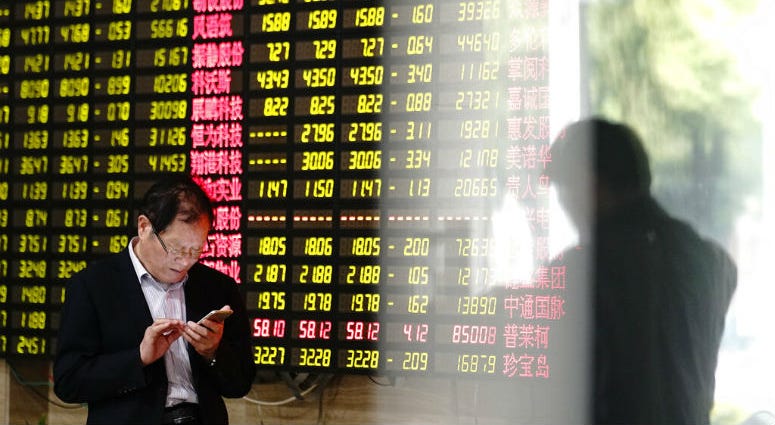 A man looks at his smartphone near a display showing stock prices at a brokerage house in Shanghai Monday, May 6, 2019. A man looks at his smartphone near a display showing stock prices at a brokerage house in Shanghai Monday, May 6, 2019.