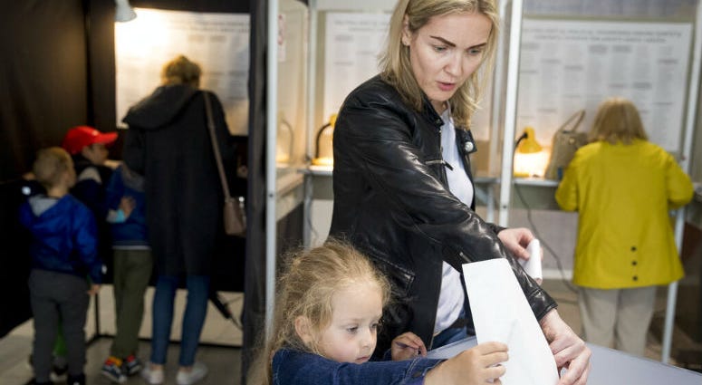 A woman with a child casts her ballot at a polling station during the second round of voting in presidential elections in Vilnius, Lithuania, Sunday, May 26, 2019. Voters are going to the polls to elect a president to succeed Dalia Grybauskaite, who has completed her maximum two terms in office.