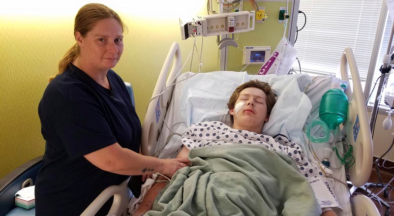 In this June 14, 2019 photo, 15-year-old Eli Gregg, right, recovers in the hospital bed in Kansas City, Kan., as his mother Jimmy Russell watches after doctors removed a 10" knife that impaled his face when he fell while playing. Eli Gregg