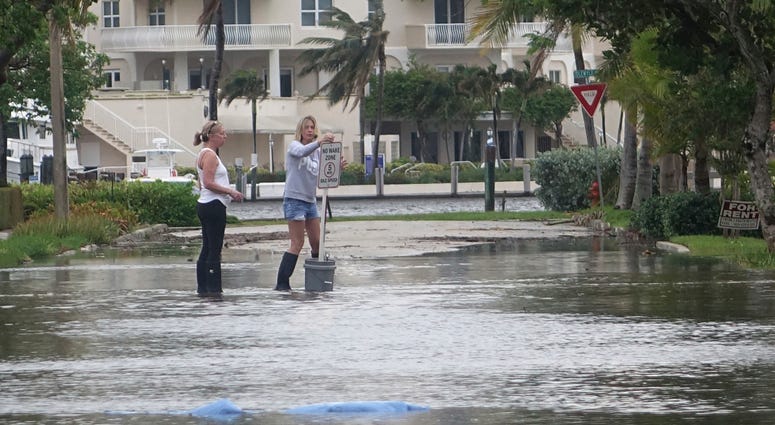 In this Oct. 5, 2017, file photo, residents move a "no wake," sign through flood waters caused by king tides in Fort Lauderdale, Fla. Flooding