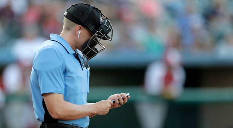 Home plate umpire Brian deBrauwere checks an iPhone while wearing an earpiece prior to the start of the Atlantic League All-Star minor league baseball game, Wednesday, July 10, 2019, in York, Pa. Umpire