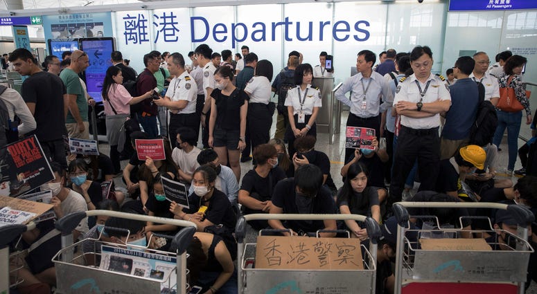 Airport security personnel stand guard as travelers walk past protesters holding a sit-in rally at the departure gate of the Hong Kong International Airport in Hong Kong, Tuesday, Aug. 13, 2019. Airport security personnel stand guard as travelers walk past protesters holding a sit-in rally at the departure gate of the Hong Kong International Airport in Hong Kong, Tuesday, Aug. 13, 2019.