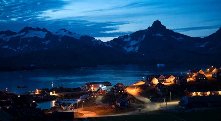 In this photo taken late Friday, Aug. 16, 2019, homes are illuminated after the sunset in Tasiilaq, Greenland. Greenland