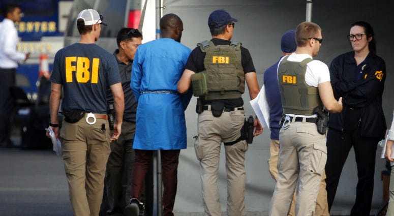 Federal agents hold a detainee, second from left, at a downtown Los Angeles parking lot after predawn raids that saw dozens of people arrested in the L.A. area Thursday, Aug. 22, 2019. U.S. authorities have unsealed a 252-count federal grand jury indictment charging 80 people with participating in a conspiracy to steal millions of dollars through a range of fraud schemes and laundering the funds through a Los Angeles-based network.