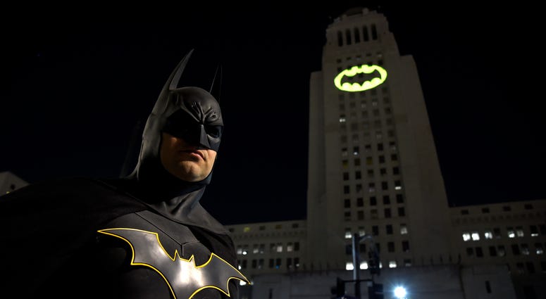 Tony Bradshaw, of Los Angeles, dressed as Batman, poses in front of a Bat-Signal projected onto City Hall during a tribute to "Batman" star Adam West in Los Angeles on June 15, 2017.