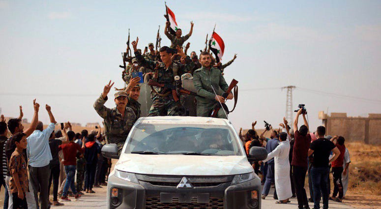 In this photo released by the Syrian official news agency SANA, people welcome Syrian troops as they enter the town of Ein Issa, north of Raqqa, Syria, Monday, Oct 14, 2019. People welcome Syrian troops