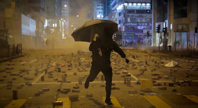 A protester with an umbrella runs away from tear gas fired by riot police on a street scattered with bricks during a protests in Hong Kong, Monday, Nov. 11, 2019. A protester with an umbrella runs away from tear gas fired by riot police on a street scattered with bricks during a protests in Hong Kong, Monday, Nov. 11, 2019.