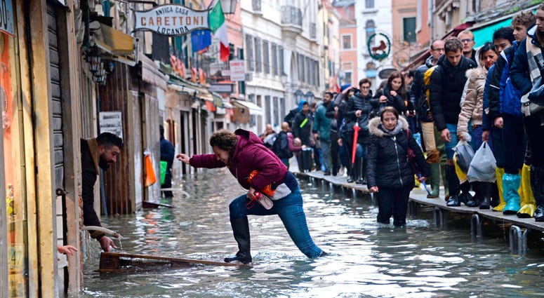 A woman tries to cross a flooded street as people walk on a trestle bridge during high water, in Venice, northern Italy, Friday, Nov. 15, 2019. A woman tries to cross a flooded street as people walk on a trestle bridge during high water, in Venice, northern Italy, Friday, Nov. 15, 2019.