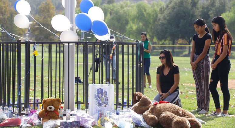 Parent Mirna Herrera kneels with her daughters Liliana, 15, and Alexandra, 16 at the Central Park memorial for the Saugus High School victims in Santa Clarita, Calif., Friday, Nov. 15, 2019. Parent Mirna Herrera kneels with her daughters Liliana, 15, and Alexandra, 16 at the Central Park memorial for the Saugus High School victims in Santa Clarita.