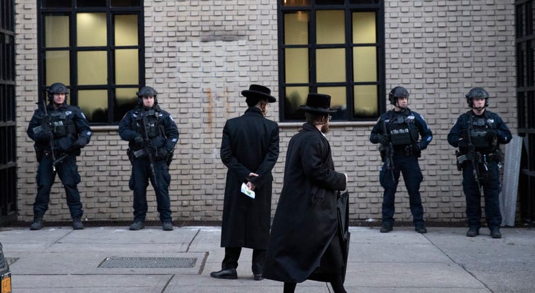 In this Dec. 11, 2019 file photo, Orthodox Jewish men pass New York City police guarding a Brooklyn synagogue prior to a funeral for Mosche Deutsch in New York. Orthodox Jewish men at a Brooklyn synagogue