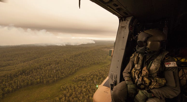 In this Sunday, Jan. 5, 2020, photo provided by Australian Department of Defence, a Royal Australian Navy MRH-90 helicopter crew member looks out over fires burning near Cann River, Australia. In this Sunday, Jan. 5, 2020, photo provided by Australian Department of Defence, a Royal Australian Navy MRH-90 helicopter crew member looks out over fires burning near Cann River, Australia.