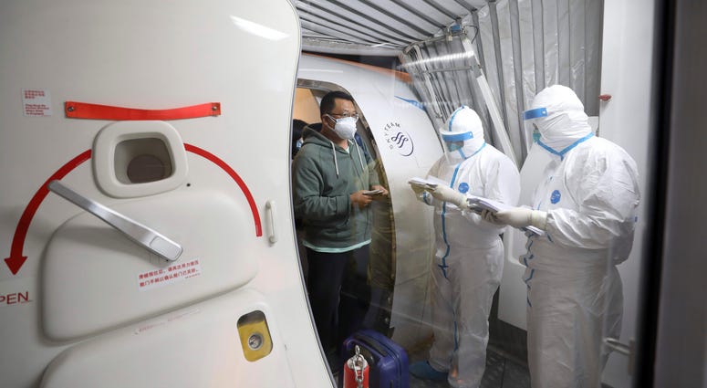Quarantine workers in protective suits check identity documents as tourists from the Wuhan area walk off of a chartered plane taking them home from Bangkok at Wuhan Tianhe International Airport in Wuhan in central China's Hubei Province, Jan. 31, 2020. Quarantine workers in protective suits