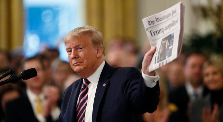 President Donald Trump holds up a newspaper with the headline that reads "Trump acquitted" as he speaks in the East Room of the White House in Washington, Thursday, Feb. 6, 2020. Trump