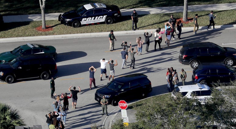In this Wednesday, Feb. 14, 2018, file photo, students hold their hands in the air as they are evacuated by police from Marjory Stoneman Douglas High School in Parkland, Fla., after a shooter opened fire on the campus. Mass shooting at Marjory Stoneman Douglas High School