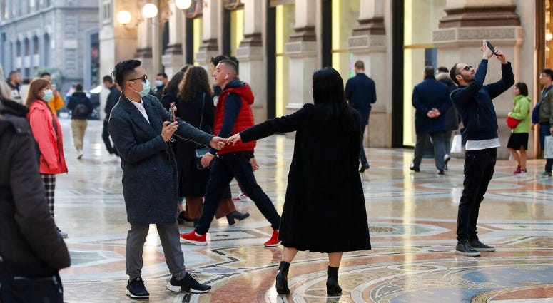 Tourists wearing sanitary masks move a few steps of dance, in downtown Milan, Italy, Sunday, Feb. 23, 2020. Tourists wearing sanitary masks move a few steps of dance, in downtown Milan, Italy, Sunday, Feb. 23, 2020.