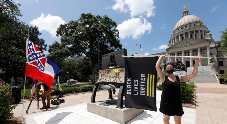 Paloma Wu holds a Black Lives Matter banner while calling for a new Mississippi state flag, while current flag supporters wave the flag as both sides make their sentiments known. Paloma Wu holds a Black Lives Matter banner while calling for a new Mississippi state flag, while current flag supporters wave the flag as both sides make their sentiments known.