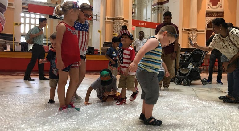 Kids at the Please Touch Museum use their bodies to make fireworks sounds for the Fourth of July by stomping on bubble wrap. Bubble Stomp Fireworks