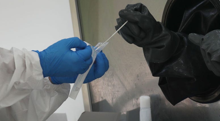 MIAMI BEACH, FLORIDA - JULY 17: A nurse receives a swab to test a person through a glass pane in the Aardvark Mobile Health’s Mobile Covid-19 Testing Truck A nurse receives a swab to test a person through a glass pane in the Aardvark Mobile Health’s Mobile Covid-19 Testing Truck