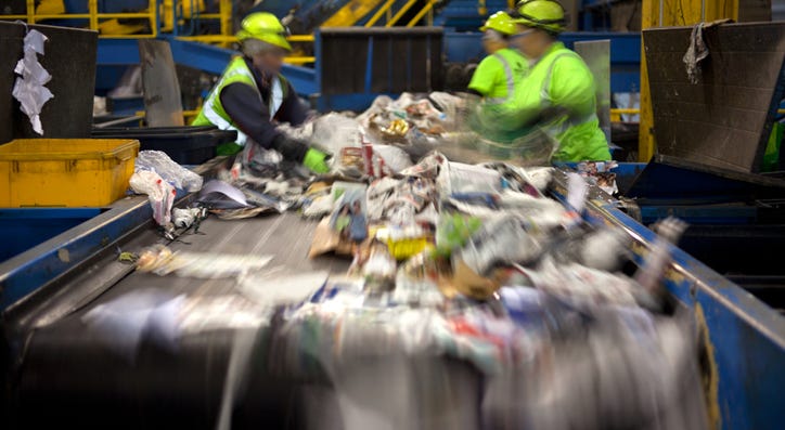 Workers separating paper and plastic on a conveyor belt in a recycling facility. Workers separating paper and plastic on a conveyor belt in a recycling facility.