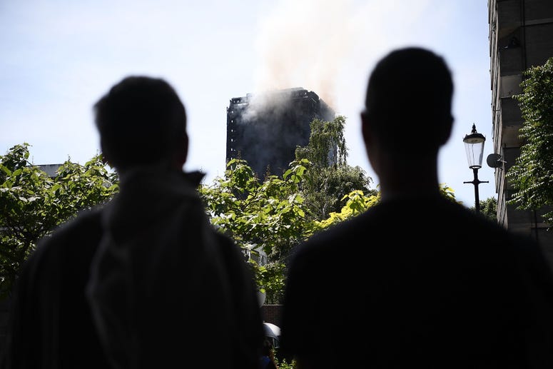 Two men watch from under the Westway near the burning 24 storey residential Grenfell Tower block in Latimer Road, West London on June 14, 2017 in London, England. Grenfell Tower fire