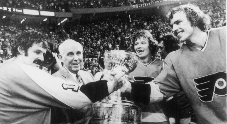 Canadian hockey players Bernie Parent (left) and Bill Clement (right) of the Philadelphia Flyers clasp hands as NHL President Clarence Campbell (second left) presents them with the Stanley Cup after their victory over the Buffalo Sabres, May 27, 1975. Flyers win Stanley Cup 1975