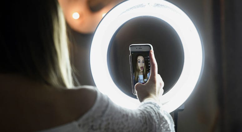 In this Feb. 28, 2018 photo, Matty Nev Luby holds up her phone in front of a ring light she uses to lip-sync with the smartphone app Musical.ly, in Wethersfield, Conn. In this Feb. 28, 2018 photo, Matty Nev Luby holds up her phone in front of a ring light she uses to lip-sync with the smartphone app Musical.ly, in Wethersfield, Conn.