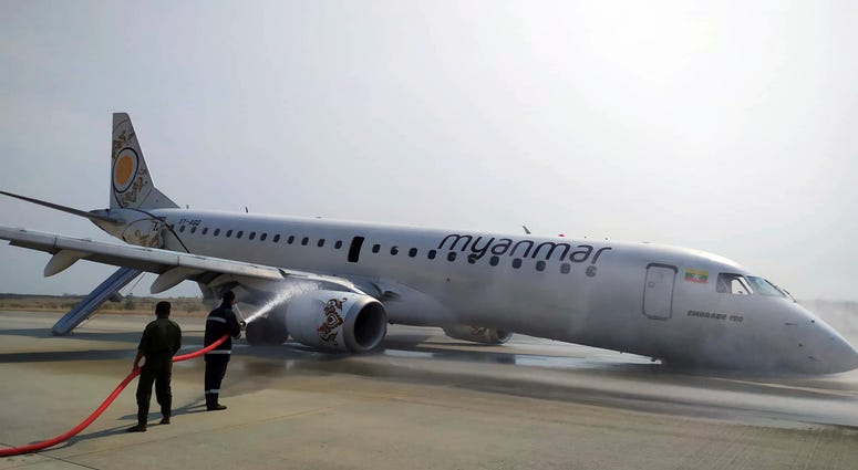 Firefighters work with hose on a plane of Myanmar National Airline (MNA) after an accident at Mandalay International airport Sunday, May 12, 2019, in Mandalay, Myanmar. All passengers and crew are reported safe and uninjured after a Myanmar National Airlines plane made a scheduled but emergency landing at Mandalay International Airport on only its rear landing wheels.