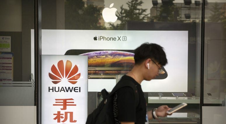 A man looks at his smartphone as he walks past an electronics shop advertising phones from Huawei and Apple in Beijing, Friday, May 24, 2019. A man looks at his smartphone as he walks past an electronics shop advertising phones from Huawei and Apple in Beijing, Friday, May 24, 2019.
