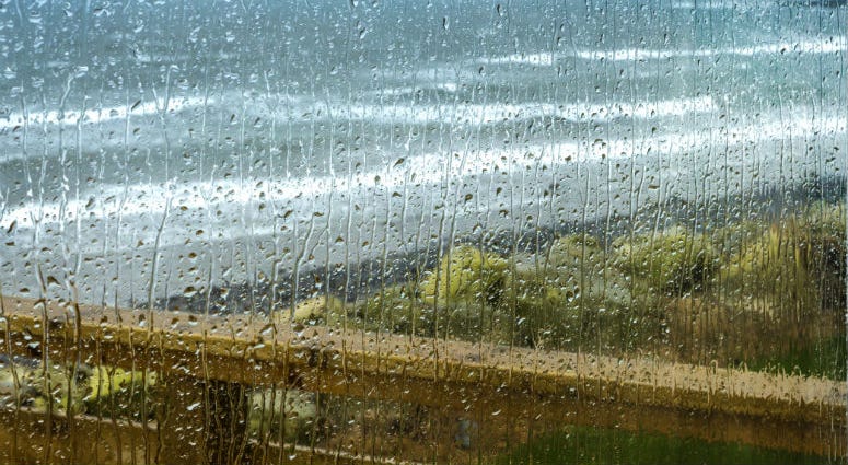 Autumn rain drops on a window, rough seas in the background. Rain