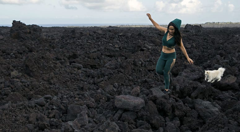 In this Monday, April 22, 2019 photo, Tisha Montoya and her dog Bebe cut through the lava field that covered much of her property and destroyed her home near Pahoa, Hawaii. In this Monday, April 22, 2019 photo, Tisha Montoya and her dog Bebe cut through the lava field that covered much of her property and destroyed her home near Pahoa, Hawaii.
