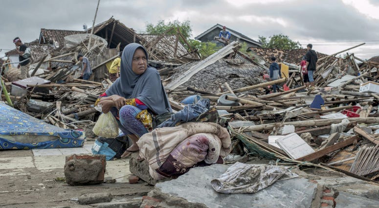 A tsunami survivor sits on a pice of debris as she salvages items from the location of her house in Sumur, Indonesia, Monday, Dec. 24, 2018. A tsunami survivor sits on a pice of debris as she salvages items from the location of her house in Sumur, Indonesia, Monday, Dec. 24, 2018.