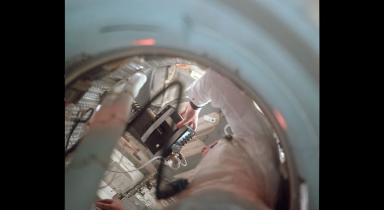 View up the tunnel towards the LM showing Neil holding the TV camera. Note how the small TV monitor has been taped to the camera body. View up the tunnel towards the LM showing Neil holding the TV camera. Note how the small TV monitor has been taped to the camera body.