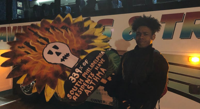 A community activist poses with signs to be used at a protest in New York City, where the PES action will occur. A community activist poses with signs to be used at a protest in New York City, where the PES action will occur.
