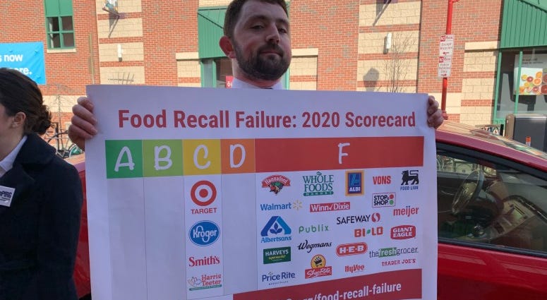 A man holds up a sign that has information on food recall failures by grocery stores. A man holds up a sign that has information on food recall failures by grocery stores.