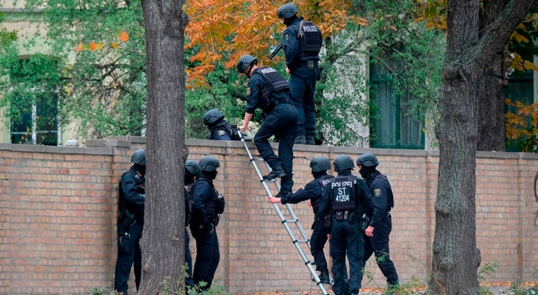 Police officers cross a wall at a crime scene in Halle, Germany, Wednesday, Oct. 9, 2019 after a shooting incident. Police officers in Halle, Germany