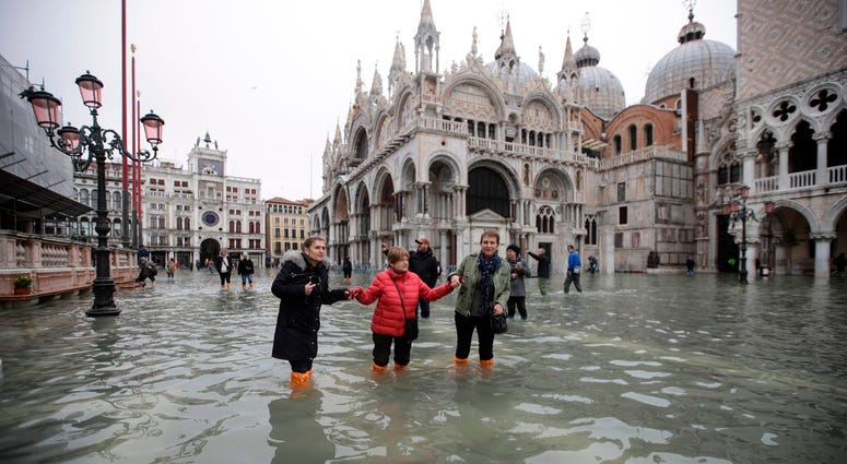 People wade through water in a flooded St. Mark's Square in Venice, Italy, Wednesday, Nov. 13, 2019. Flooding in Venice