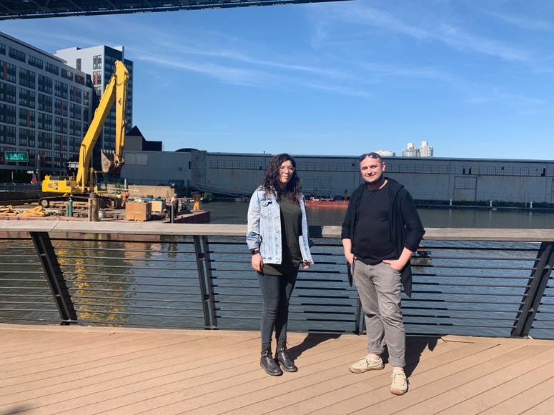 Daiana Folea (left) and Mihai Baba (right), artists for Biangle Studio, stand on the Race Street Pier in front of the half-constructed visual art installation "Ghost Ship" in the Delaware River. Ghost Ship