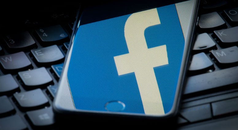 The logo of social networking site Facebook is reflected on the screen of a smartphone resting on a laptop keyboard.