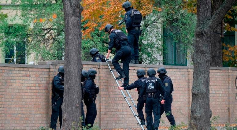 Police officers cross a wall at a crime scene in Halle, Germany, Wednesday, Oct. 9, 2019 after a shooting incident. Police officers in Halle, Germany