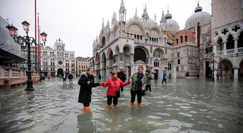 People wade through water in a flooded St. Mark's Square in Venice, Italy, Wednesday, Nov. 13, 2019. Flooding in Venice