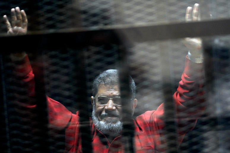 Former Egyptian President Mohammed Morsi, wearing a red jumpsuit that designates he has been sentenced to death, raises his hands inside a defendants cage in a makeshift courtroom at the national police academy, June 21, 2015, Cairo, Egypt. Egyptian President Mohammed Morsi