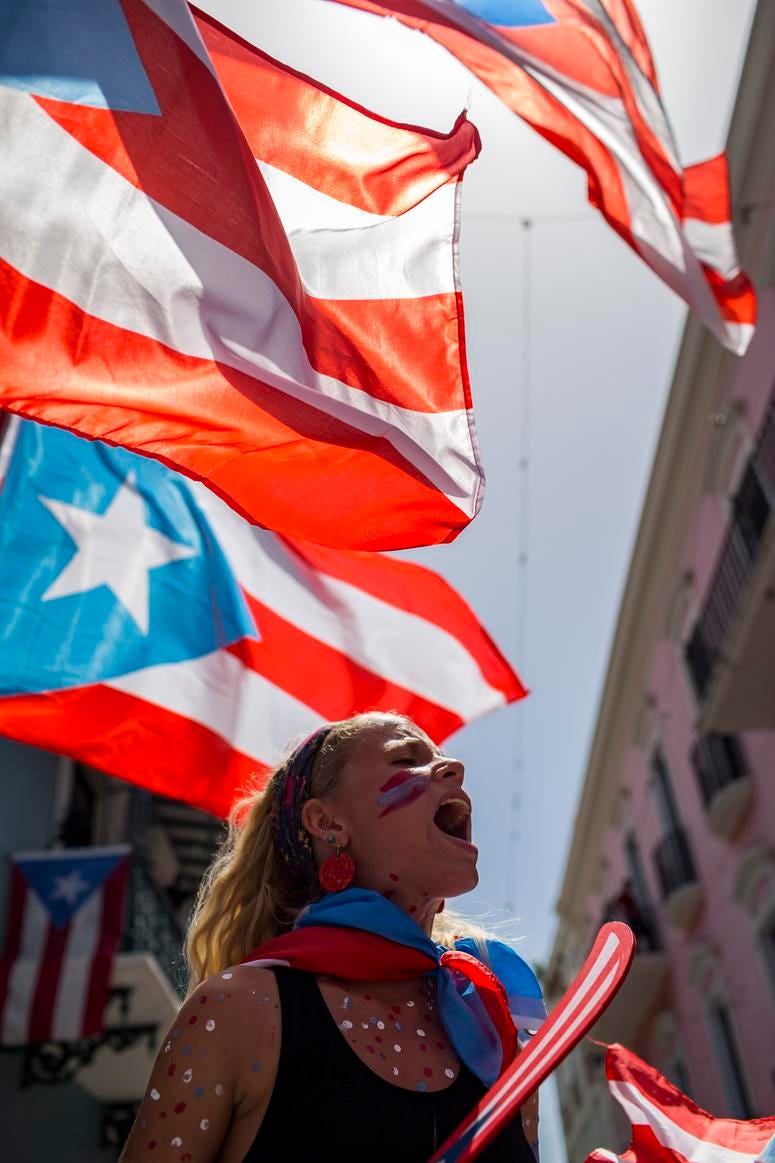 A demonstrator, Puerto Rican national flags waving above her, protests in front of the governor's mansion La Fortaleza, in San Juan, Puerto Rico, Wednesday, July 24, 2019. Puerto Rico protests