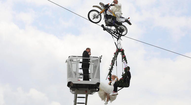 Pastor Stefan Gierung, left, stands in a cage atop of a fire service ladder in front of bride Nicole Backhaus, center, and groom Jens Knorr, right, both sitting in a swing dangling under a motorcycle. German Tightrope Wedding
