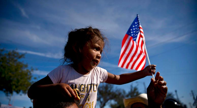 A migrant girl with a U.S. flag sits on the shoulders of a man marching with other migrants to the Chaparral border crossing in Tijuana, Mexico, Sunday, Nov. 25, 2018, as they try to reach the U.S. A migrant girl with a U.S. flag sits on the shoulders of a man marching with other migrants to the Chaparral border crossing in Tijuana, Mexico, Sunday, Nov. 25, 2018, as they try to reach the U.S.