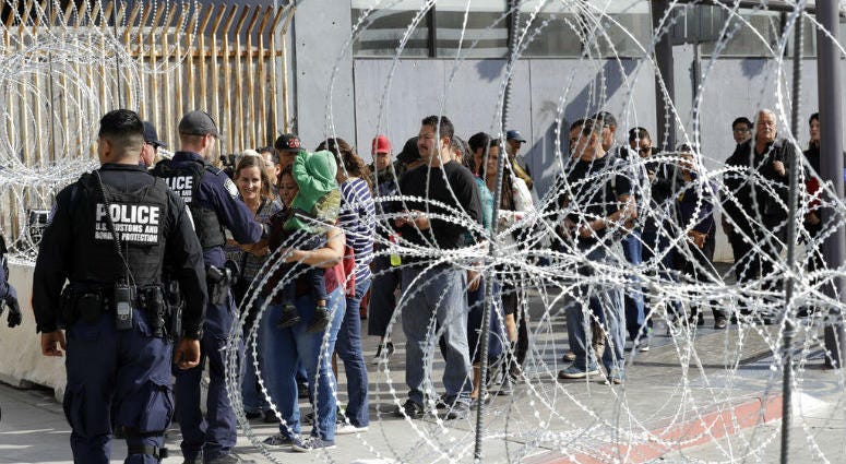 FILE - In this Nov. 19, 2018, file photo, people line up to cross into the United States from Tijuana, Mexico, seen through barriers topped with concertina wire at the San Ysidro port of entry in San Diego. FILE - In this Nov. 19, 2018, file photo, people line up to cross into the United States from Tijuana, Mexico, seen through barriers topped with concertina wire at the San Ysidro port of entry in San Diego.