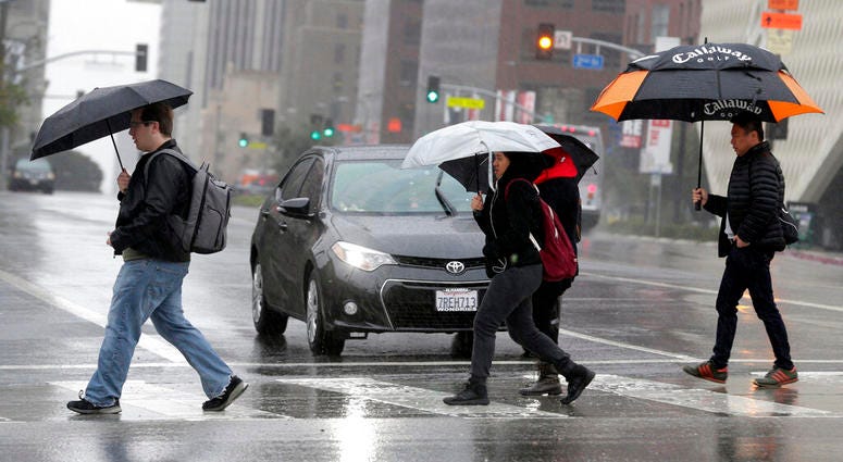 FILE - In this Monday, Feb. 6, 2017 file photo, pedestrians cross a rainy street in downtown Los Angeles. According to a study released in April 2019 in the Bulletin of the American Meteorological Society, even light rain significantly increases the risk of a fatal car crash.
