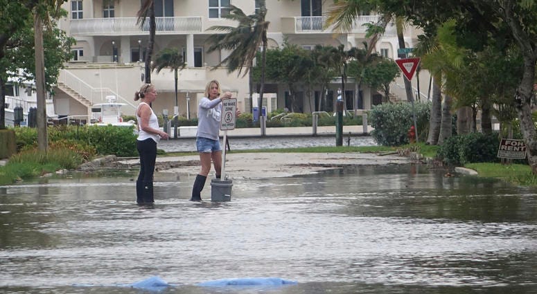 In this Oct. 5, 2017, file photo, residents move a "no wake," sign through flood waters caused by king tides in Fort Lauderdale, Fla. Flooding